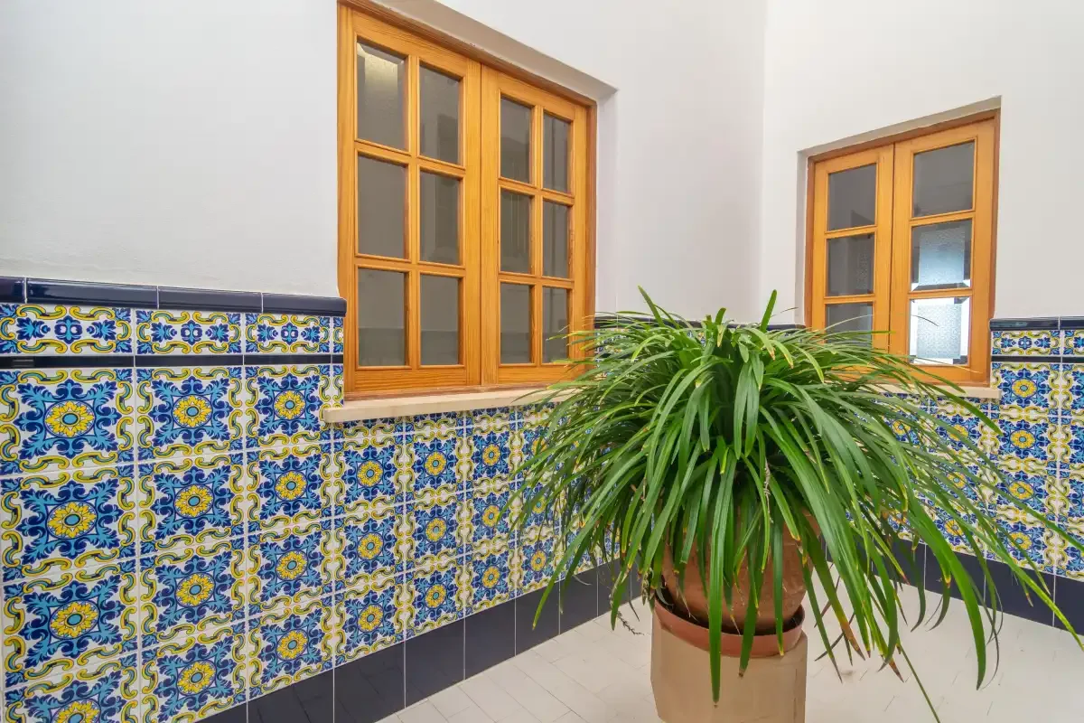 A tiled indoor courtyard features wooden-framed windows and a potted plant.
