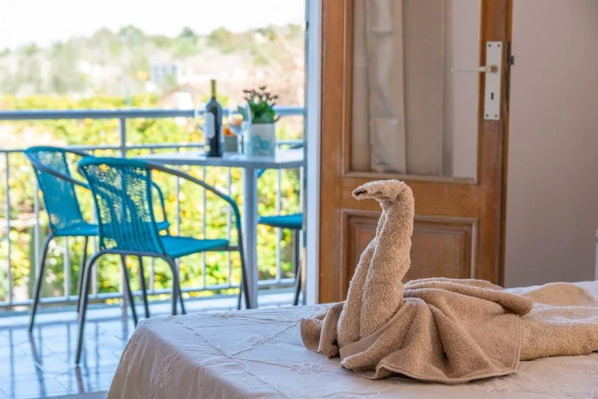 A bedroom opens onto a balcony with outdoor seating and a towel folded on the bed.