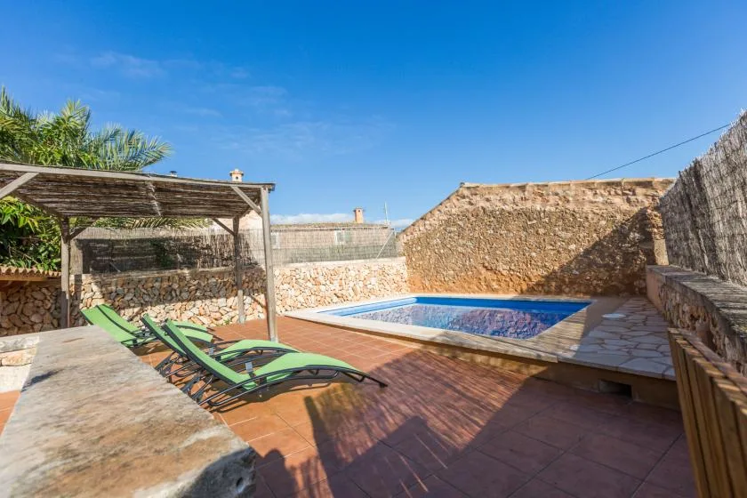A sunny outdoor pool area with green loungers beside stone walls.