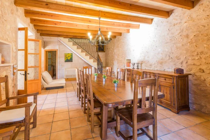A rustic dining room with a long wooden table beneath exposed ceiling beams.