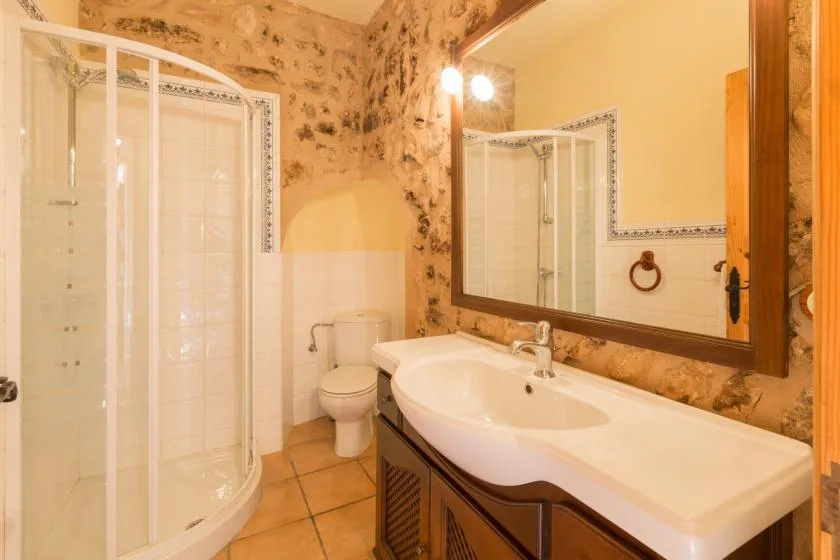 A bathroom with a curved glass shower, toilet, and long sink.
