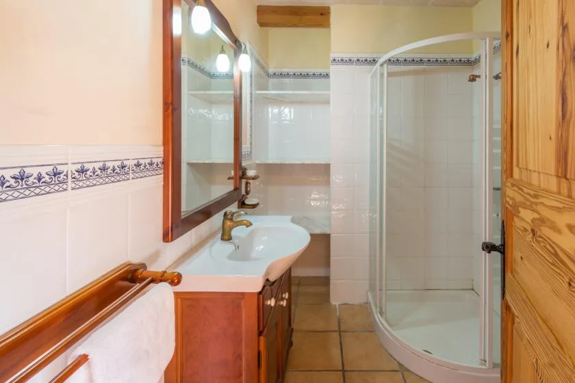 A tiled bathroom has a sink, mirror, and curved glass shower.
