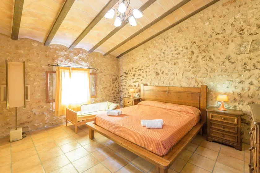 A bedroom with a wooden bed, orange bedding, and exposed ceiling beams.