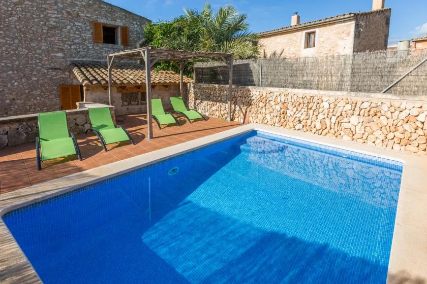 An outdoor swimming pool beside a stone patio with green loungers.