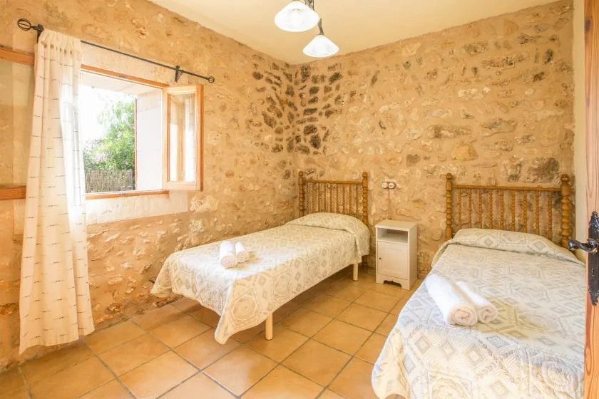 A bedroom with two single beds and a window set in stone walls.