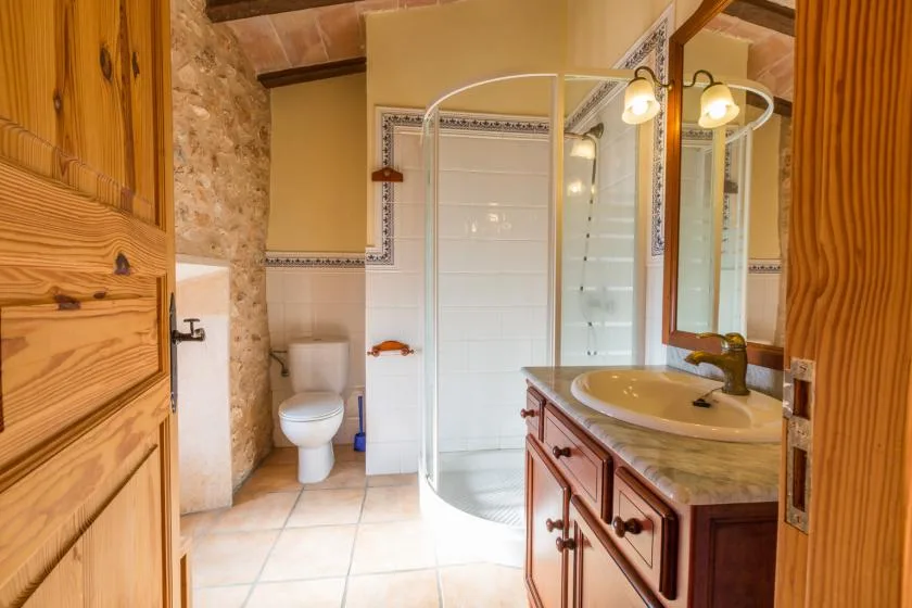 A bathroom with a curved glass shower, toilet, and sink vanity.