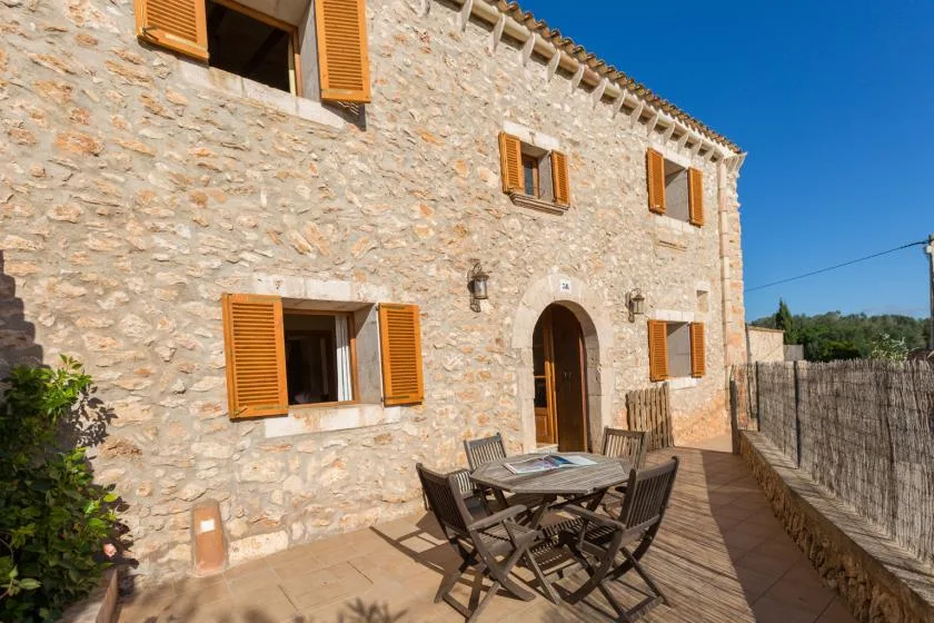 A stone house exterior with shuttered windows and a patio seating area.