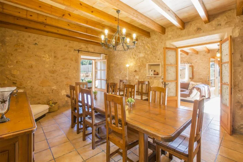 A rustic dining room with a long wooden table beneath exposed ceiling beams.