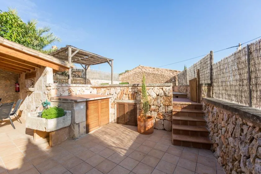 A stone-paved outdoor patio has wooden steps, a small table, and surrounding stone walls.