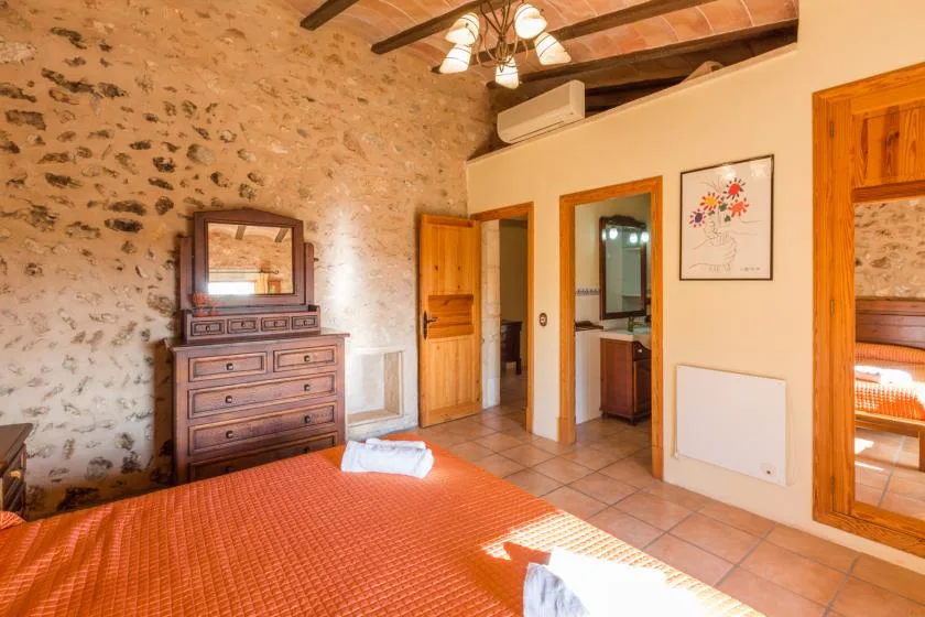 A bedroom with a tiled bed, wooden dresser, and exposed stone wall.
