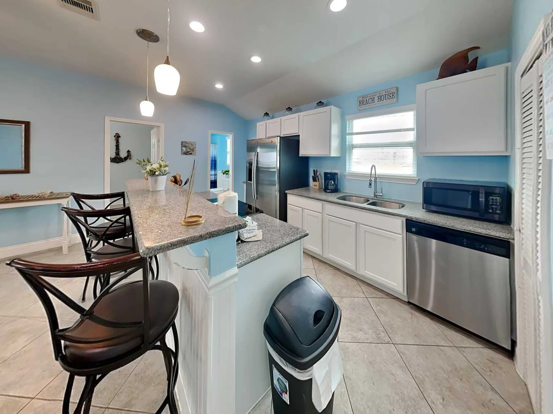 A bright kitchen with a central island, dark seating, and stainless steel appliances.