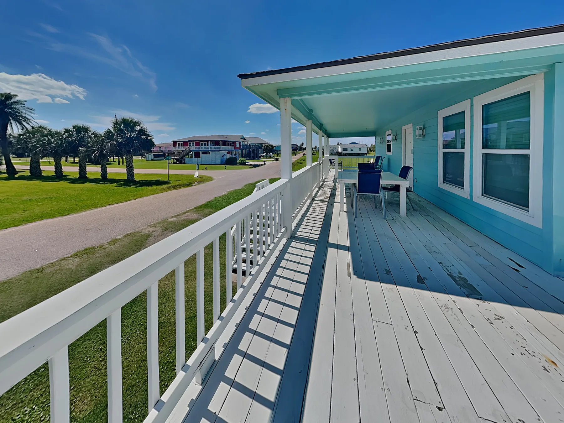 A covered porch with white railings and seating overlooks a grassy lawn.