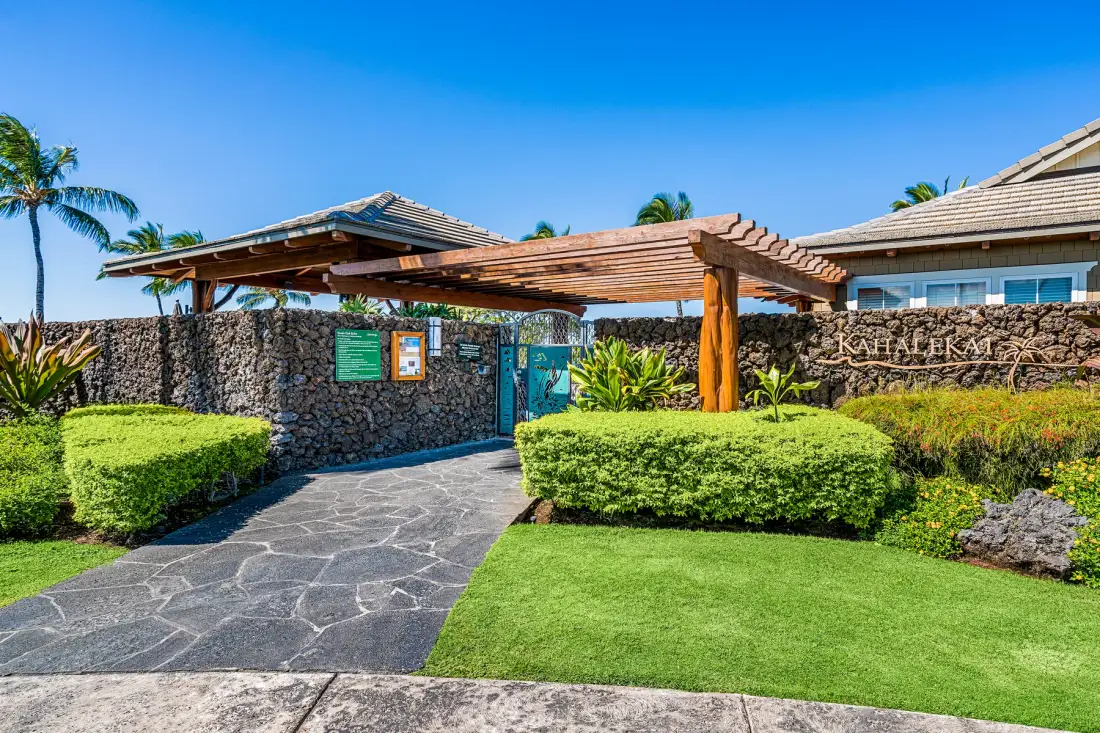 Un camino ajardinado pasa bajo una pérgola de madera junto a un muro de piedra.