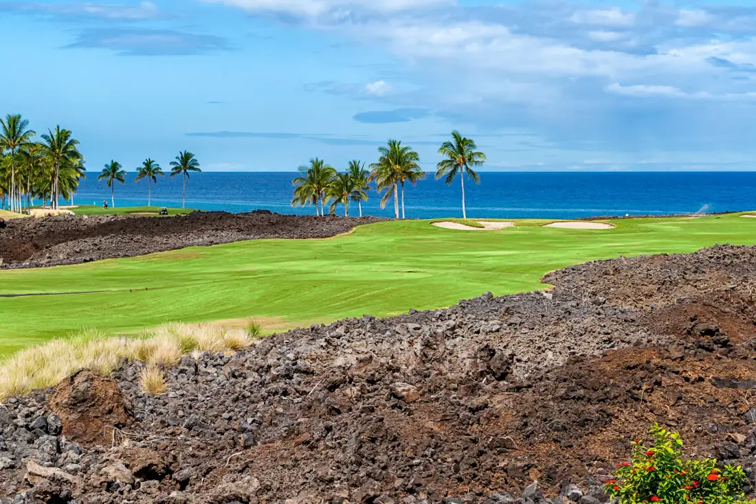 Un campo de golf costero se extiende hacia el océano, con palmeras junto a la costa.