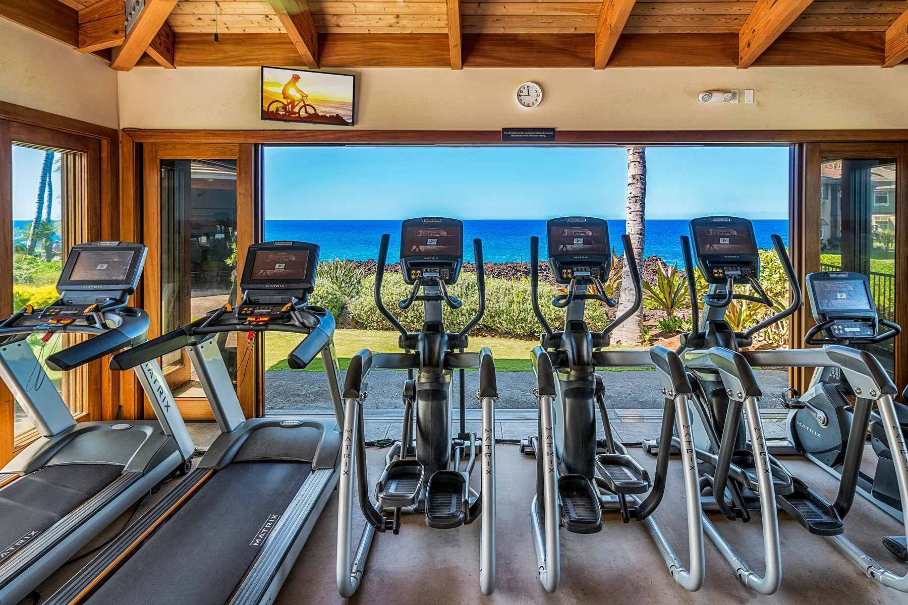 Un gimnasio con cintas de correr y máquinas elípticas frente a una amplia vista al mar.