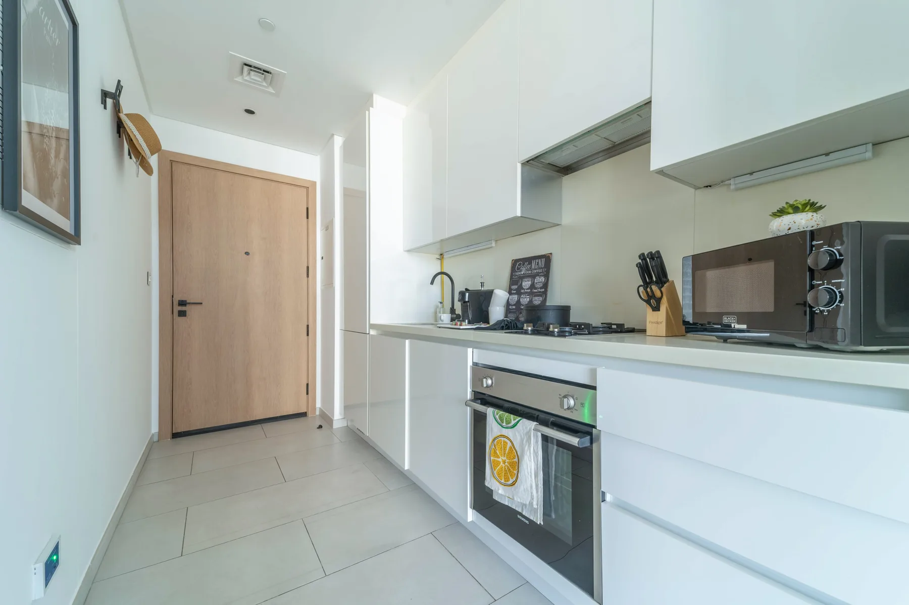 A bright, modern kitchen with white cabinetry and a wooden entry door.