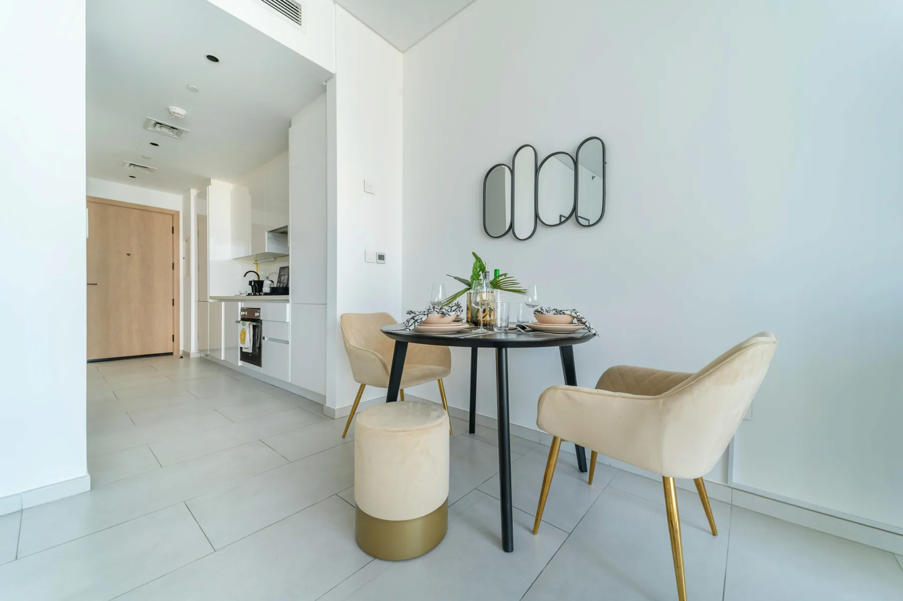A dining area with a round table, upholstered seating, and a compact kitchen behind it.