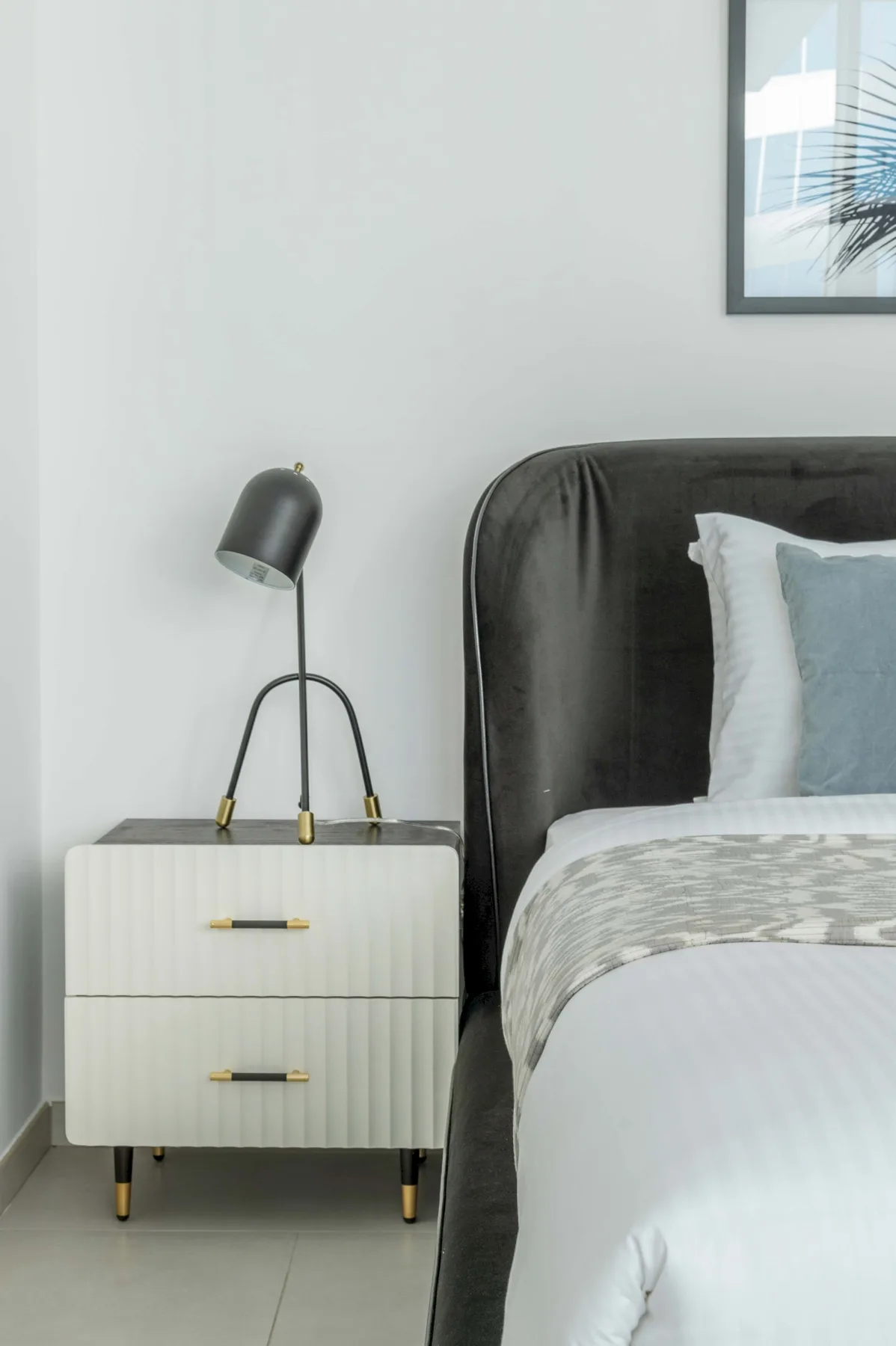A bedroom with a bed beside a white bedside table and lamp.