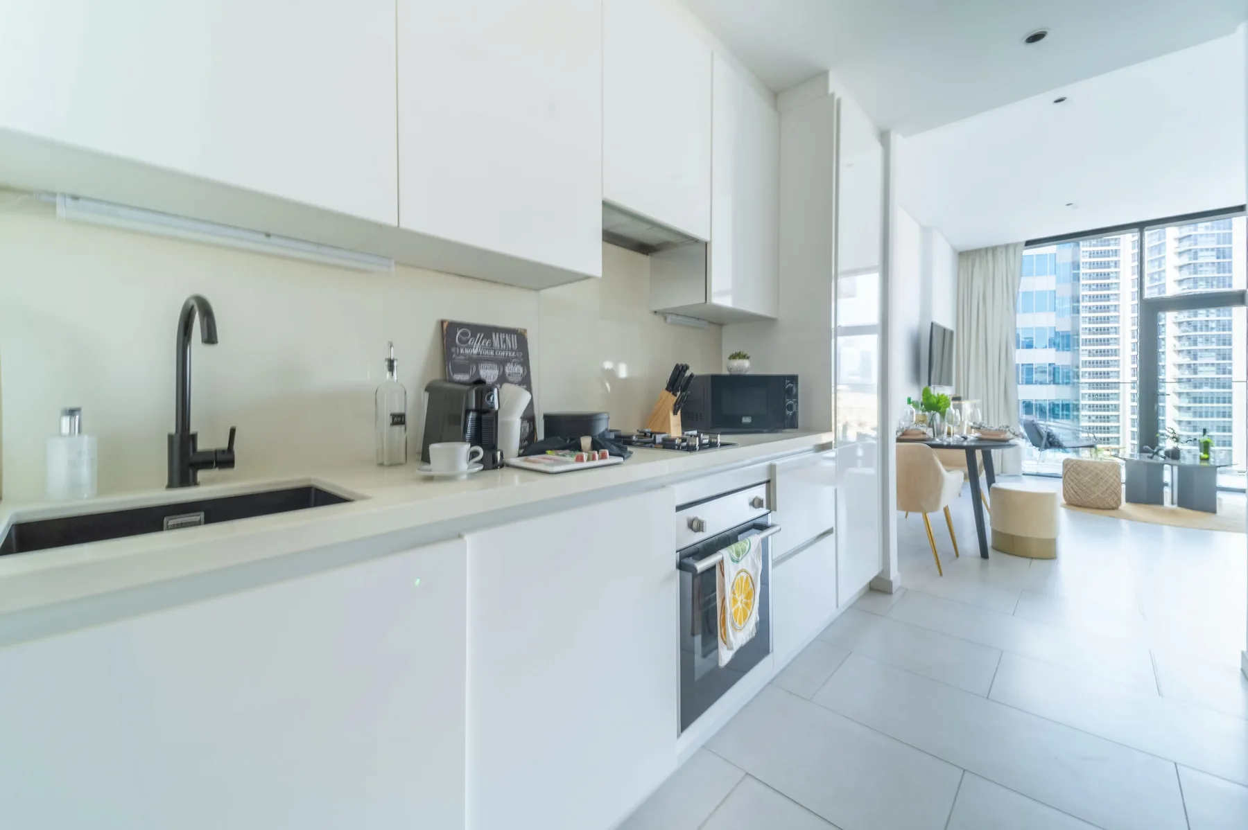 A bright modern kitchen opens onto a dining and living area with large windows.