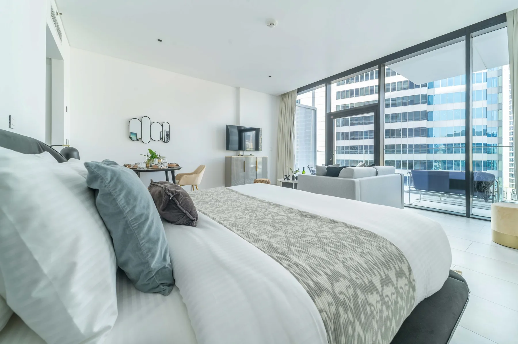 A bright bedroom with a bed, a seating area, and large windows.
