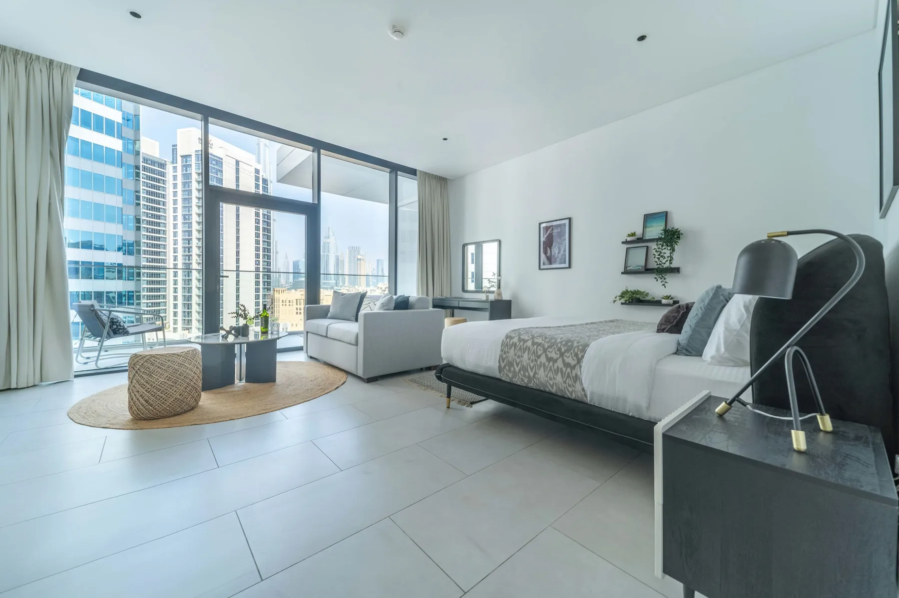 Un dormitorio luminoso con cama, zona de estar y ventanales.