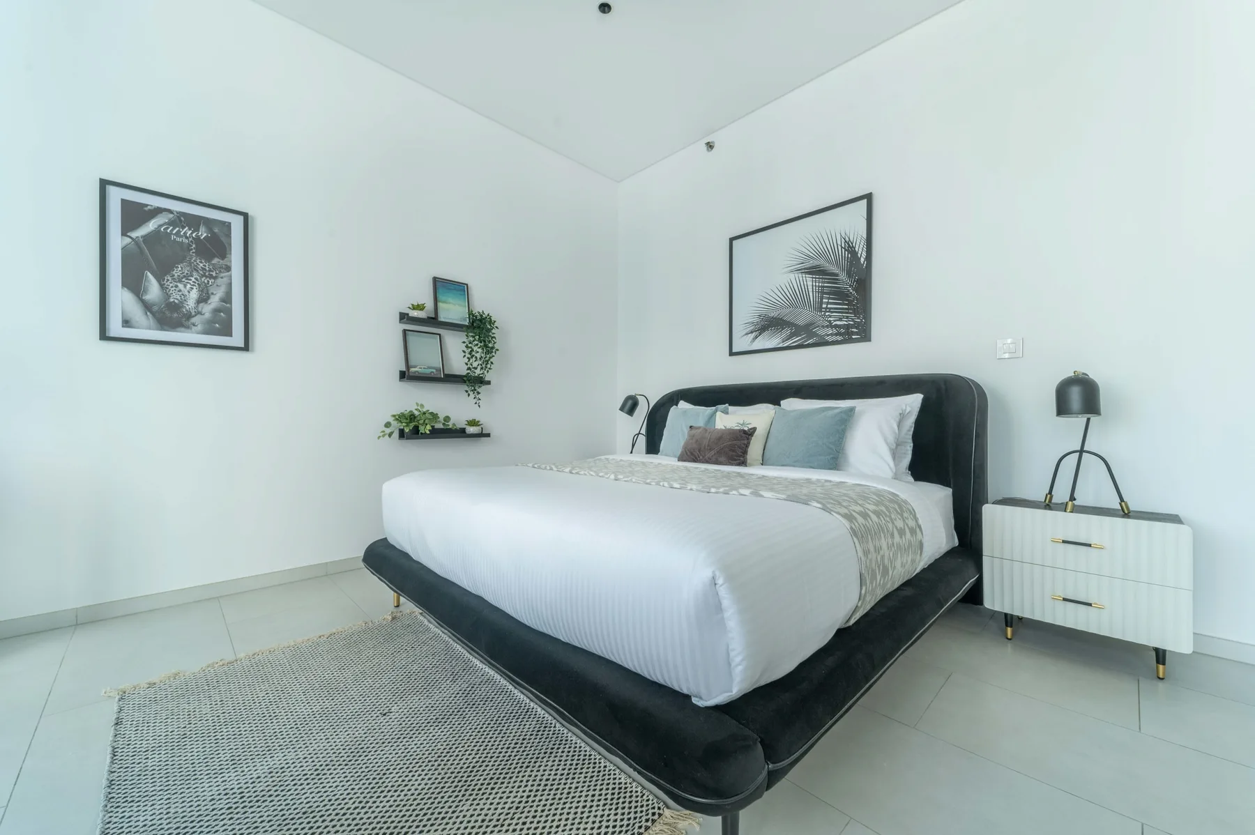 A bright bedroom with a neatly made bed and framed wall art.