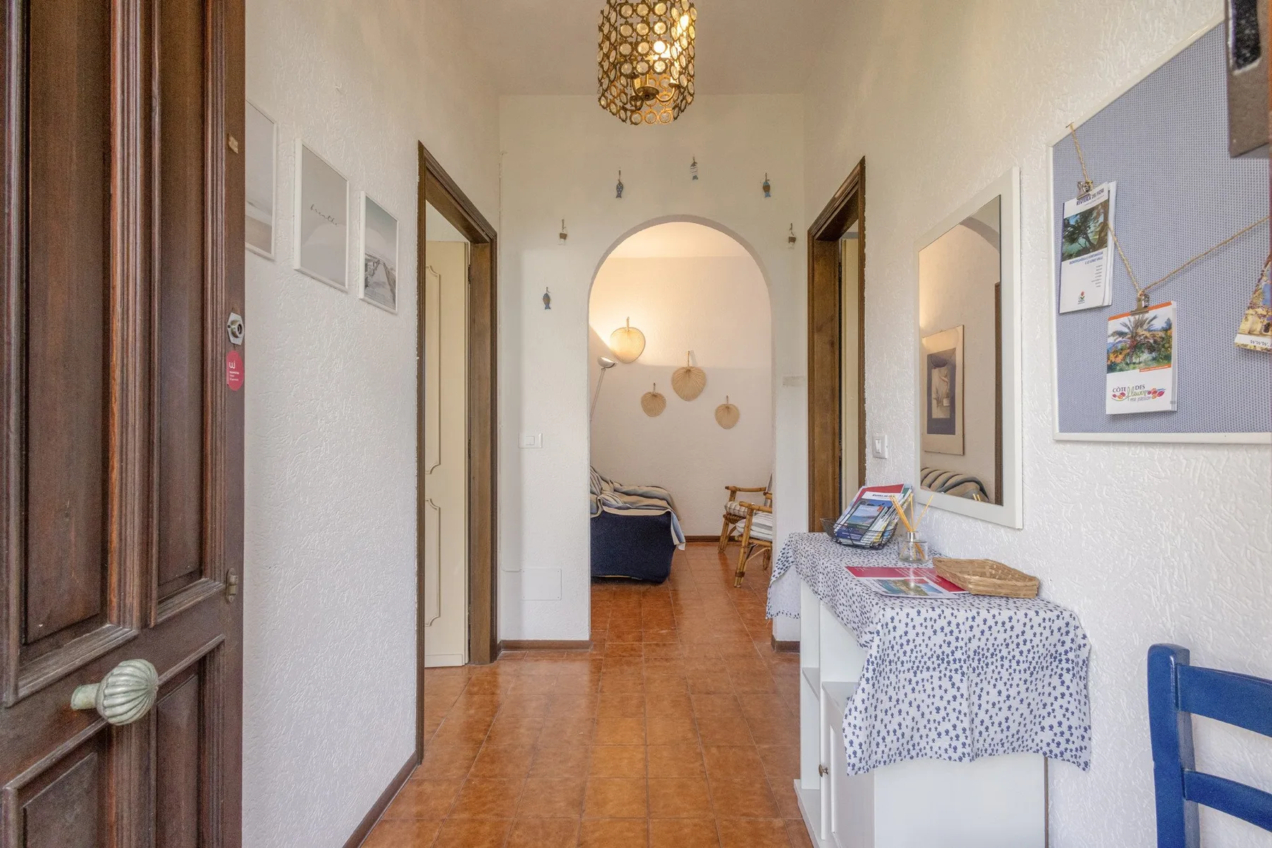 A bright hallway leads through an archway to a room with seating.