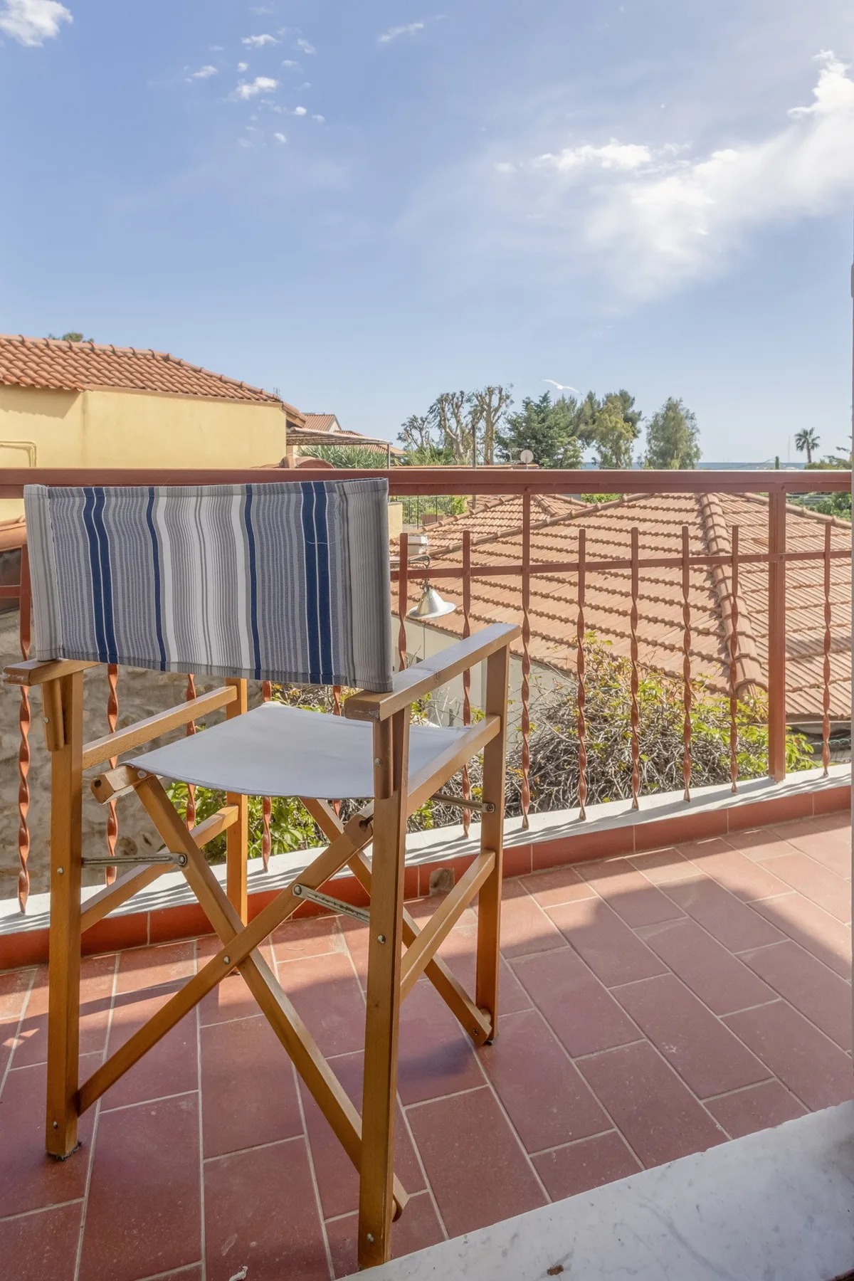 A tiled rooftop terrace has a wooden chair beside a metal railing.