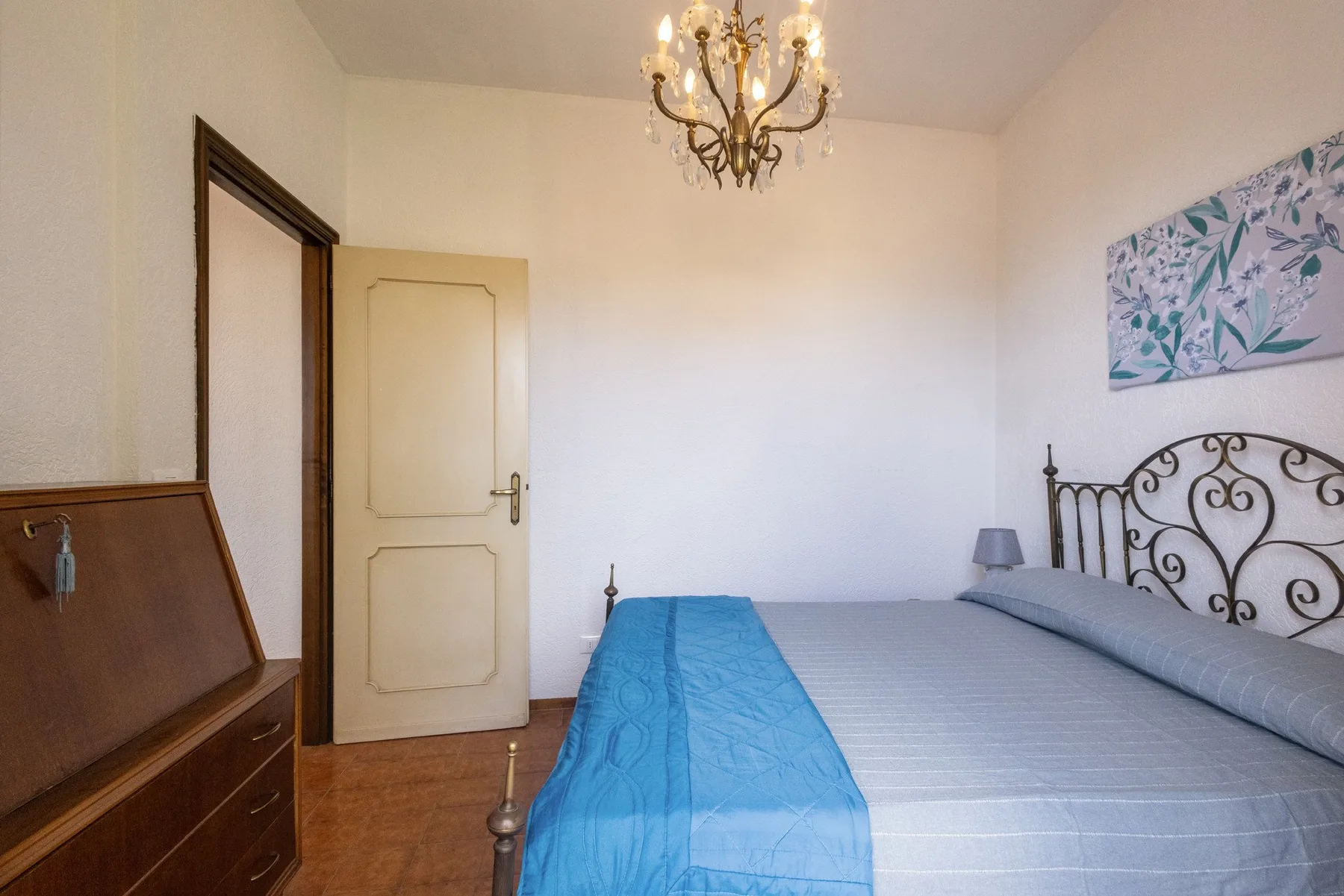 A bedroom with a bed, a chandelier, and framed artwork on the wall.