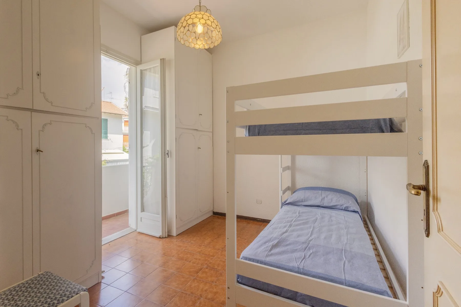A bedroom with a bunk bed, built-in cabinets, and an open balcony door.