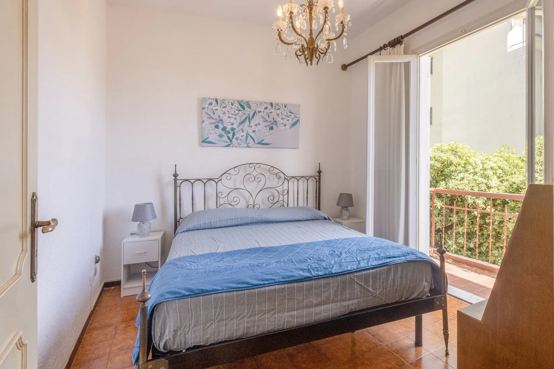 A bedroom with a metal bed, blue bedding, and open doors to a balcony.