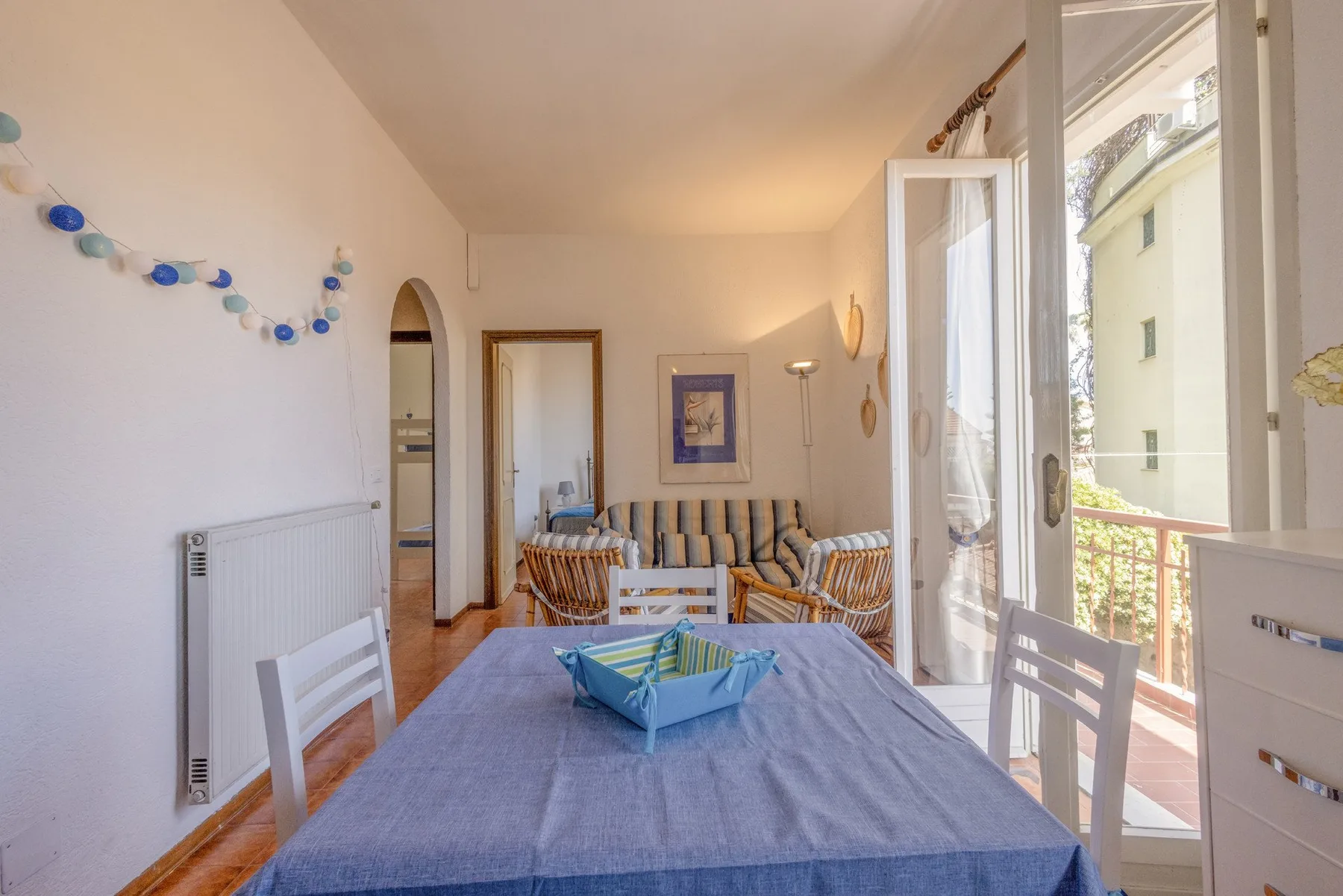 A dining area with a set table and striped seating beside open balcony doors.