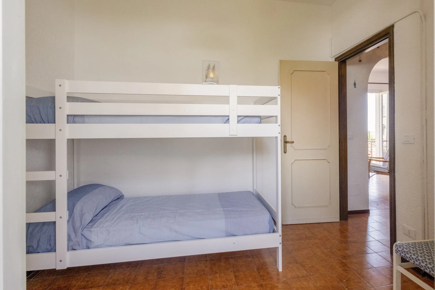 A bedroom with a white bunk bed and a doorway leading to a bright adjoining room.