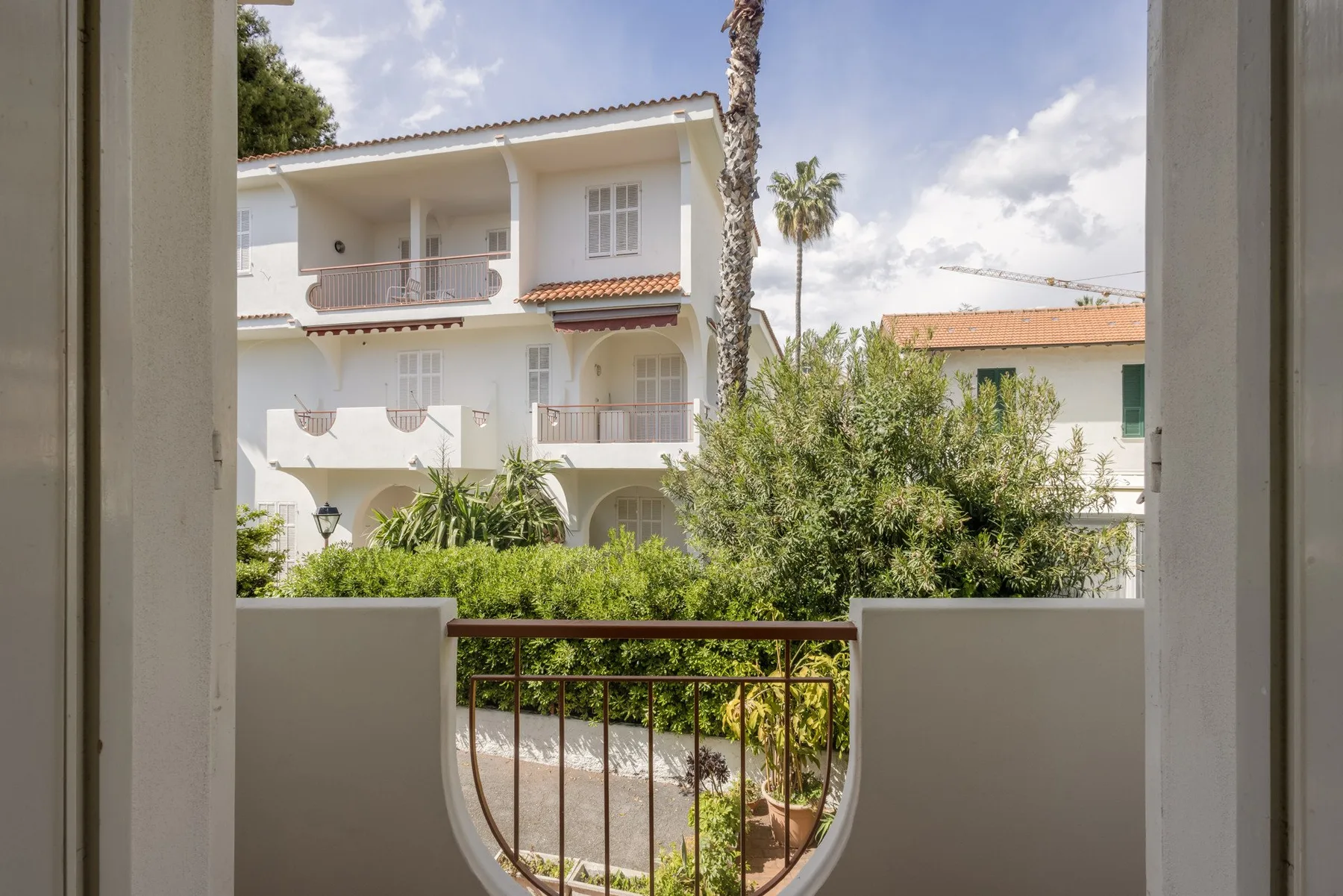 A balcony overlooks leafy shrubs and neighboring white buildings.
