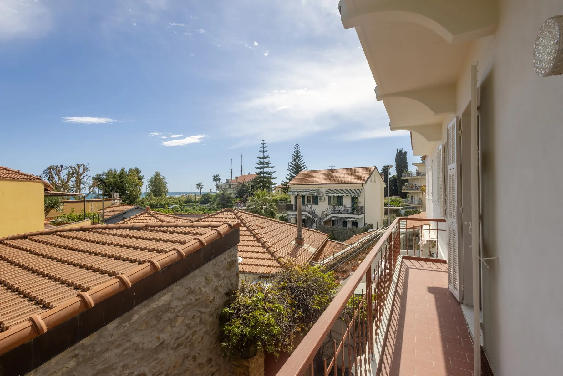 A narrow outdoor balcony overlooks tiled rooftops and nearby houses.