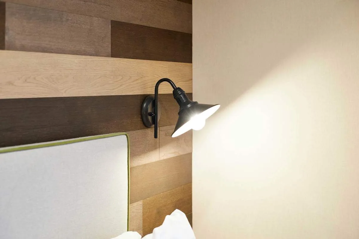 Un cabecero de dormitorio con una lámpara de lectura fijada a la pared junto a la cama.