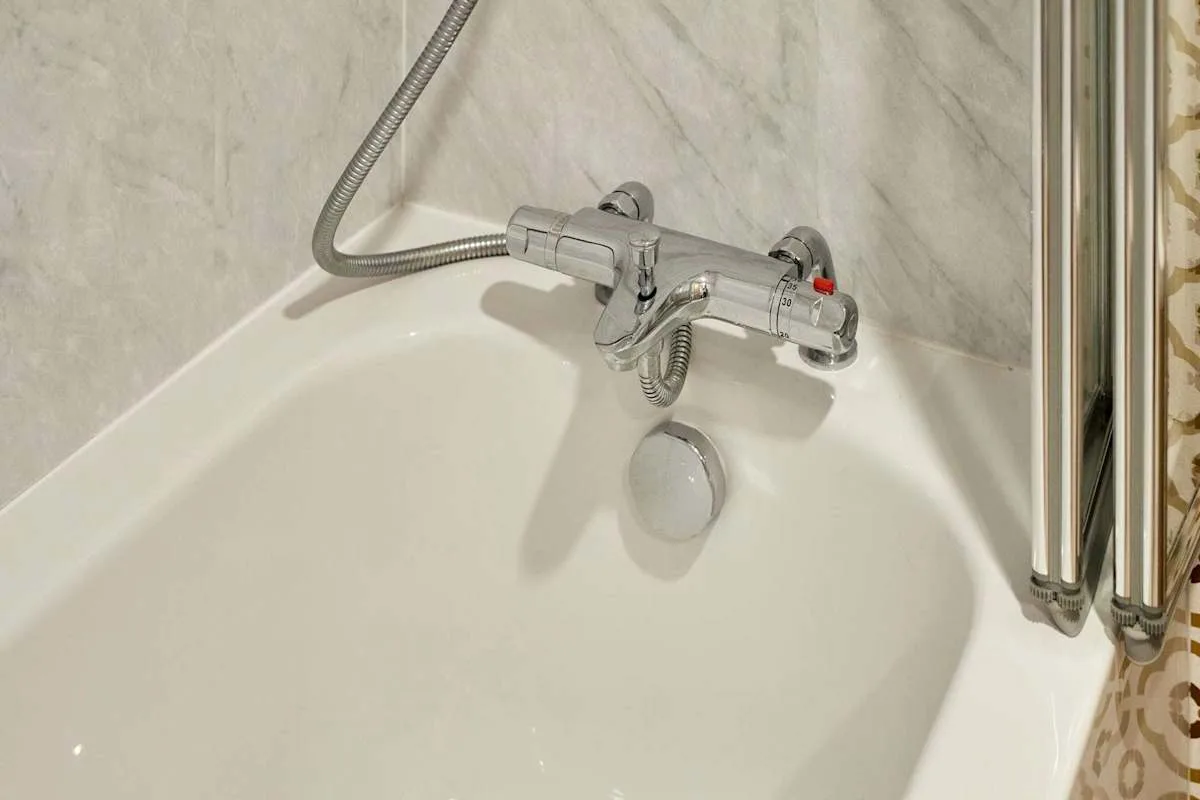 Una bañera con grifo de pared y ducha de mano.