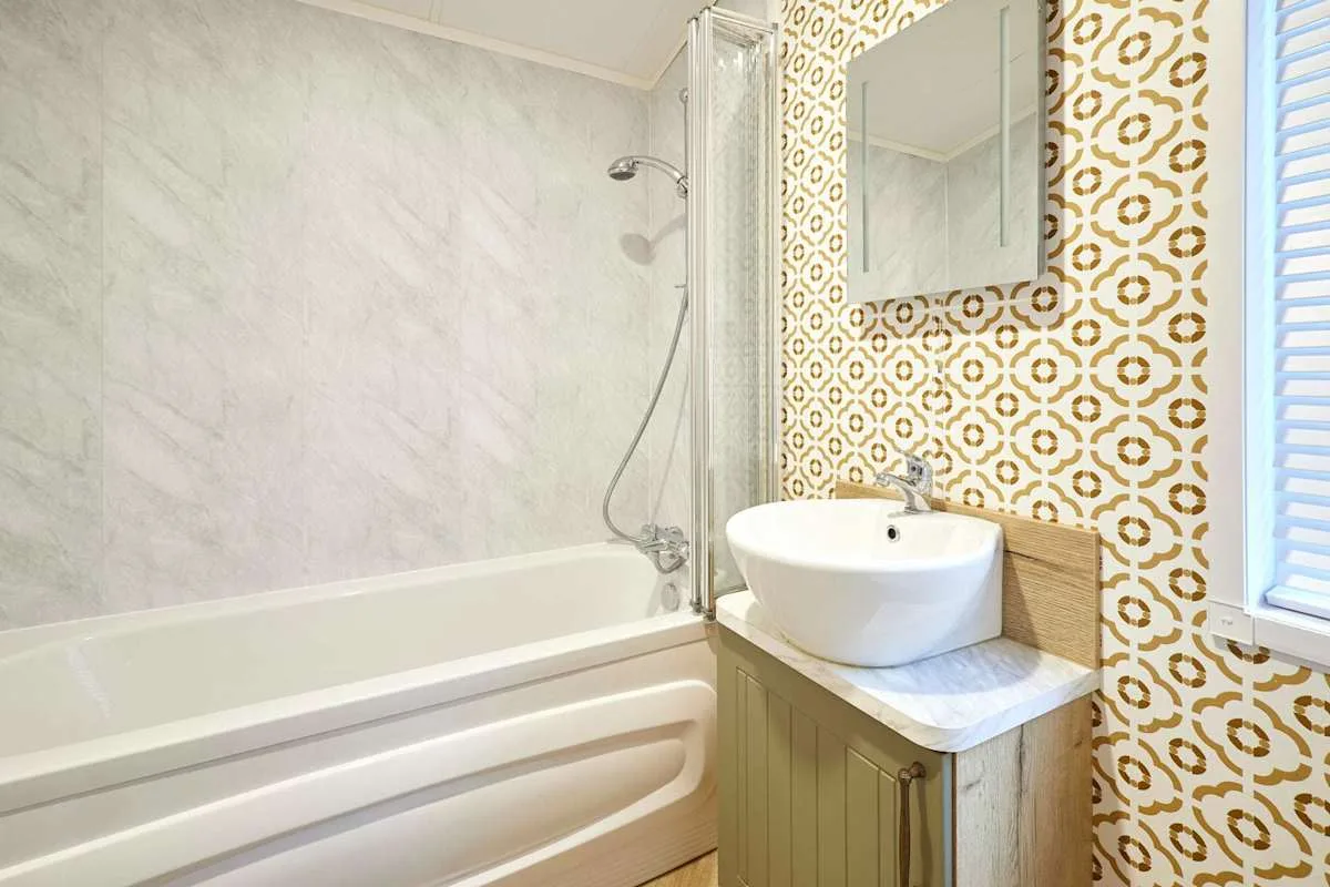 Un baño con bañera, ducha y lavabo junto a papel tapiz estampado.