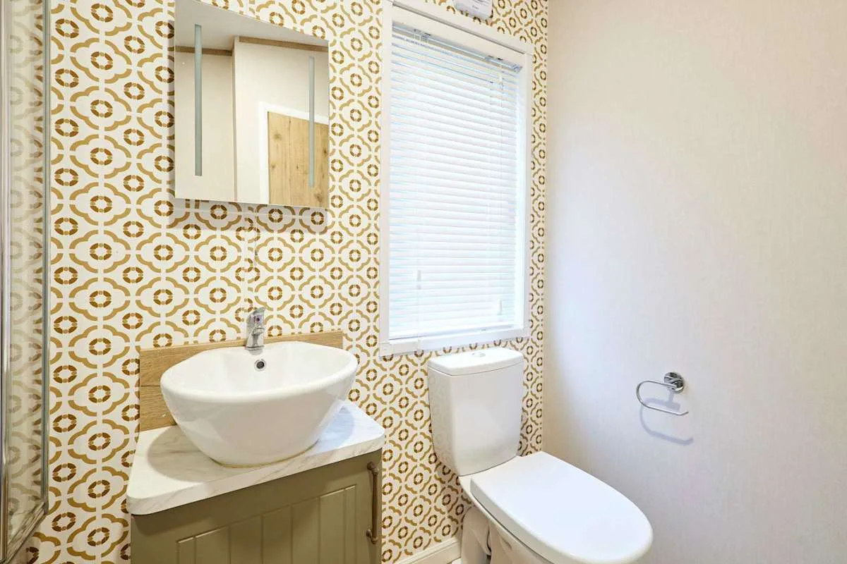 Un baño con lavabo sobre encimera, inodoro y papel tapiz estampado.