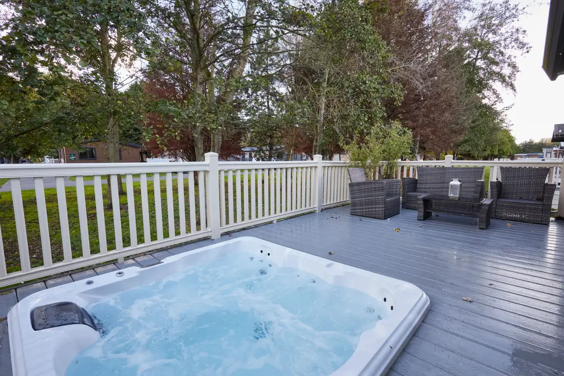 An outdoor deck with a bubbling hot tub and seating beside a white railing.