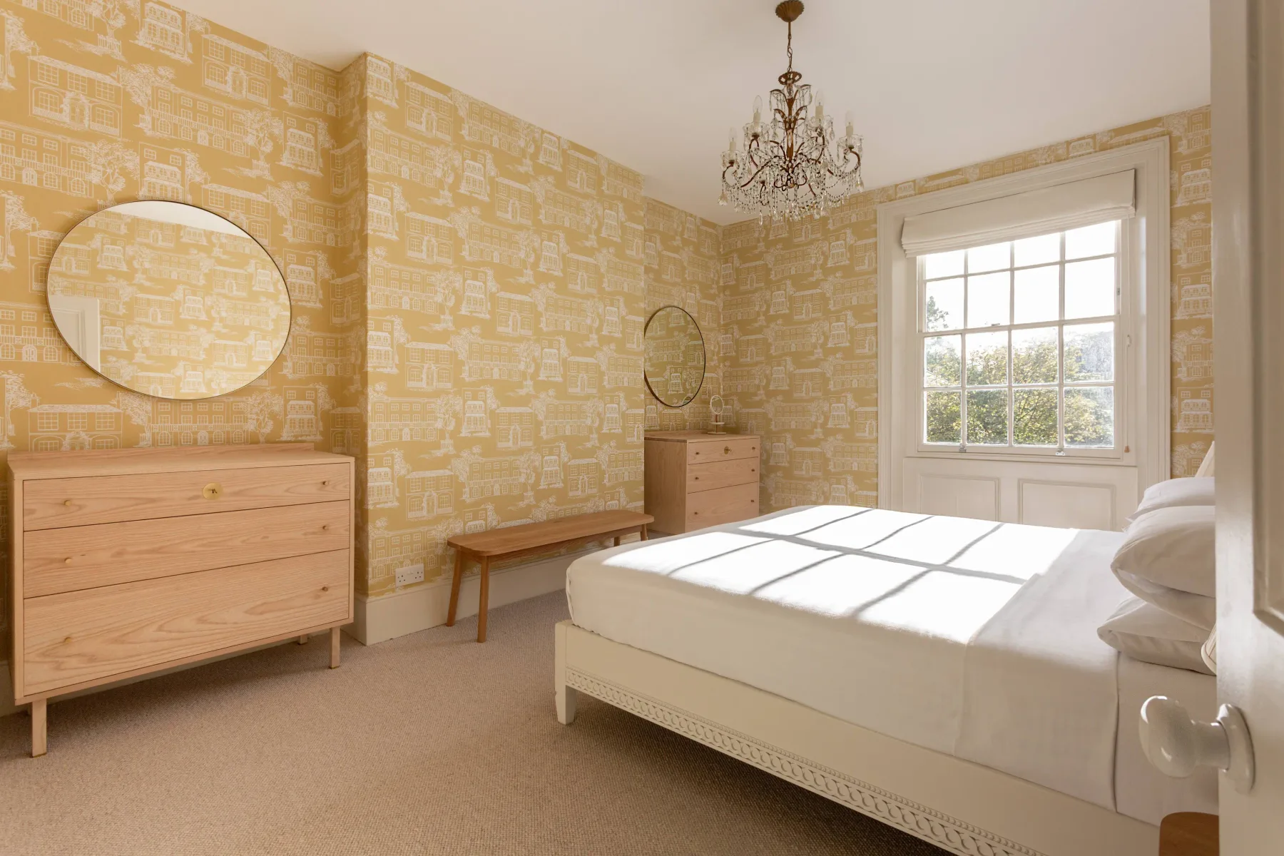 A bright bedroom with a large bed, patterned wallpaper, and a window.