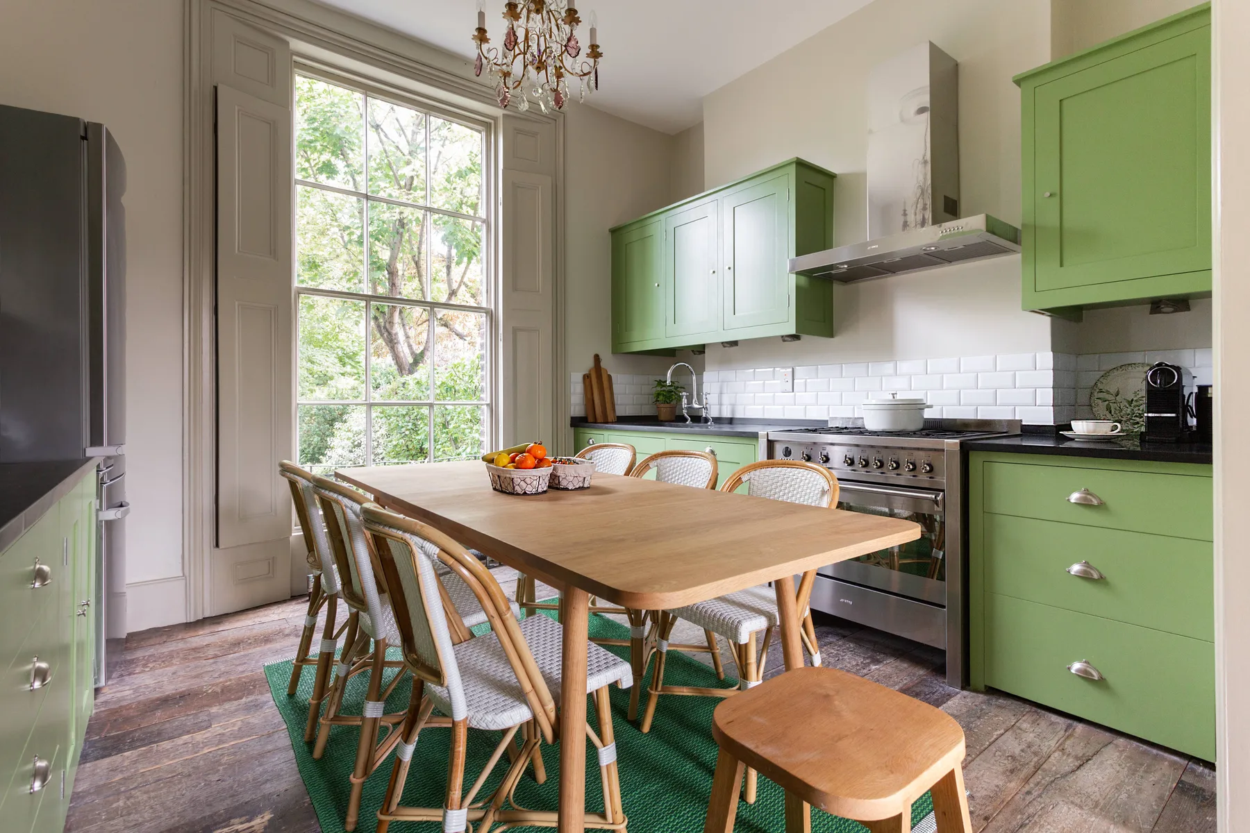 A kitchen with green cabinets, a wooden dining table, and a large window.