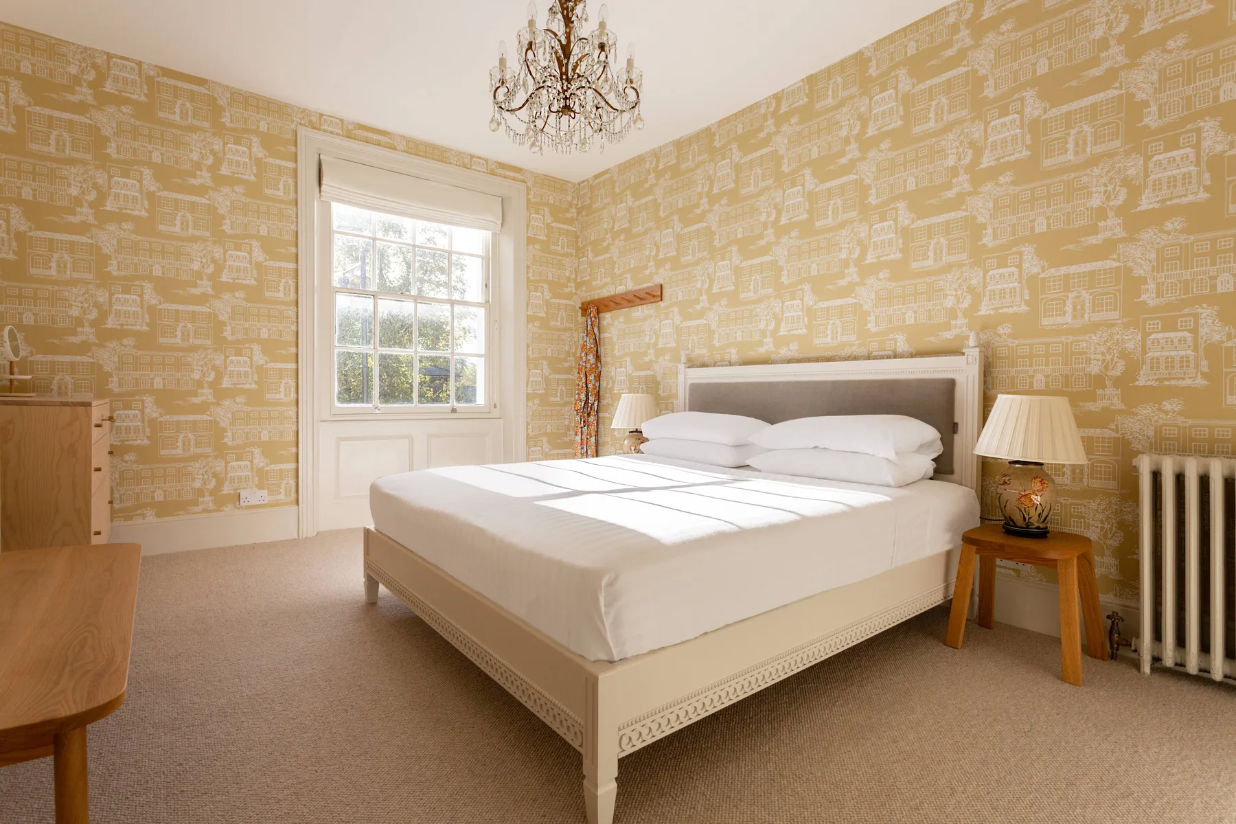 A bedroom with a white bed, patterned wallpaper, and a window.