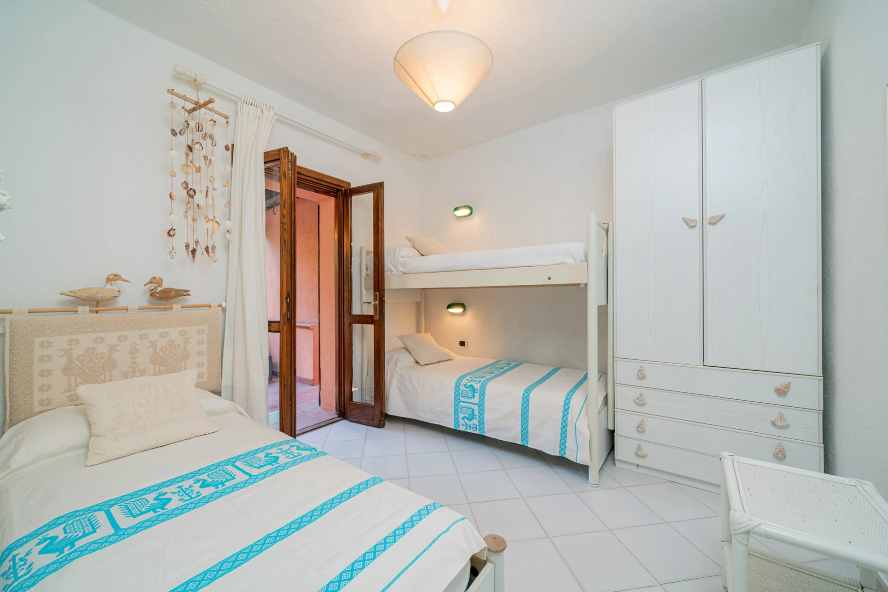 Un dormitorio luminoso con camas, ropa de cama blanca y detalles estampados turquesa.