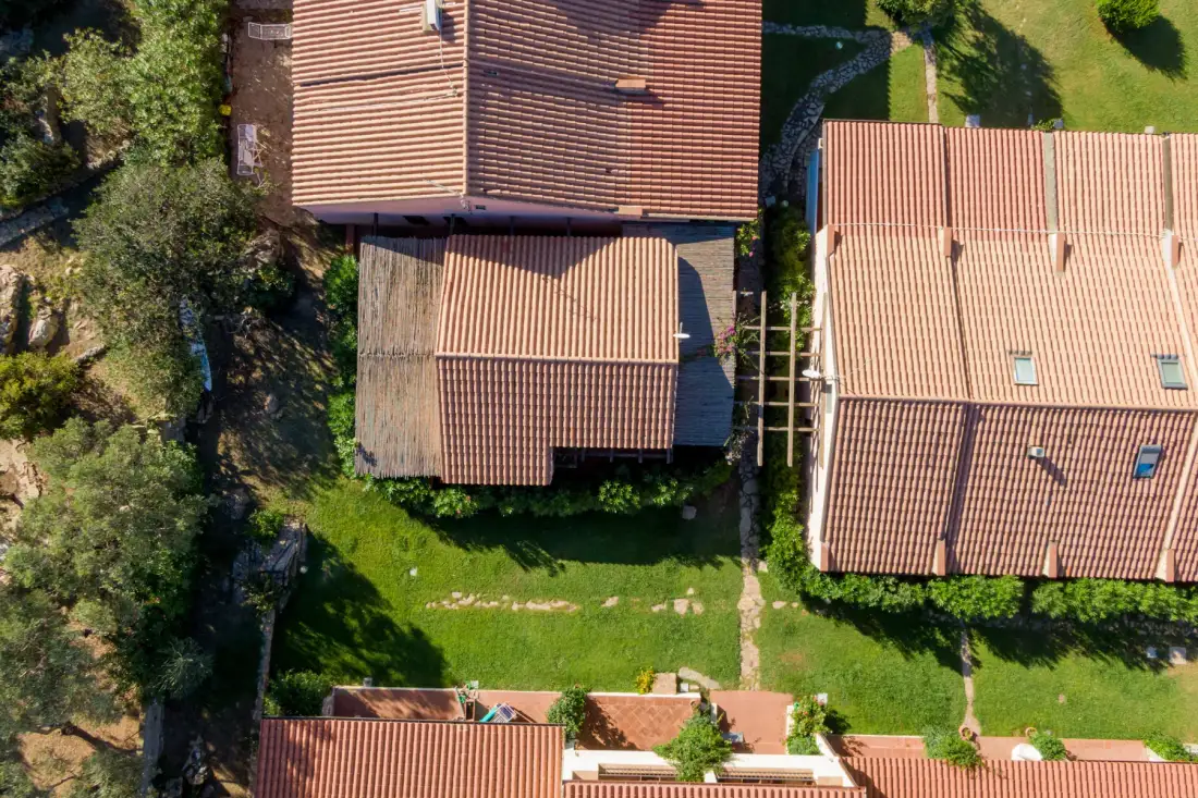 Aerial view of several terracotta-tiled rooftops surrounded by green lawns and trees.