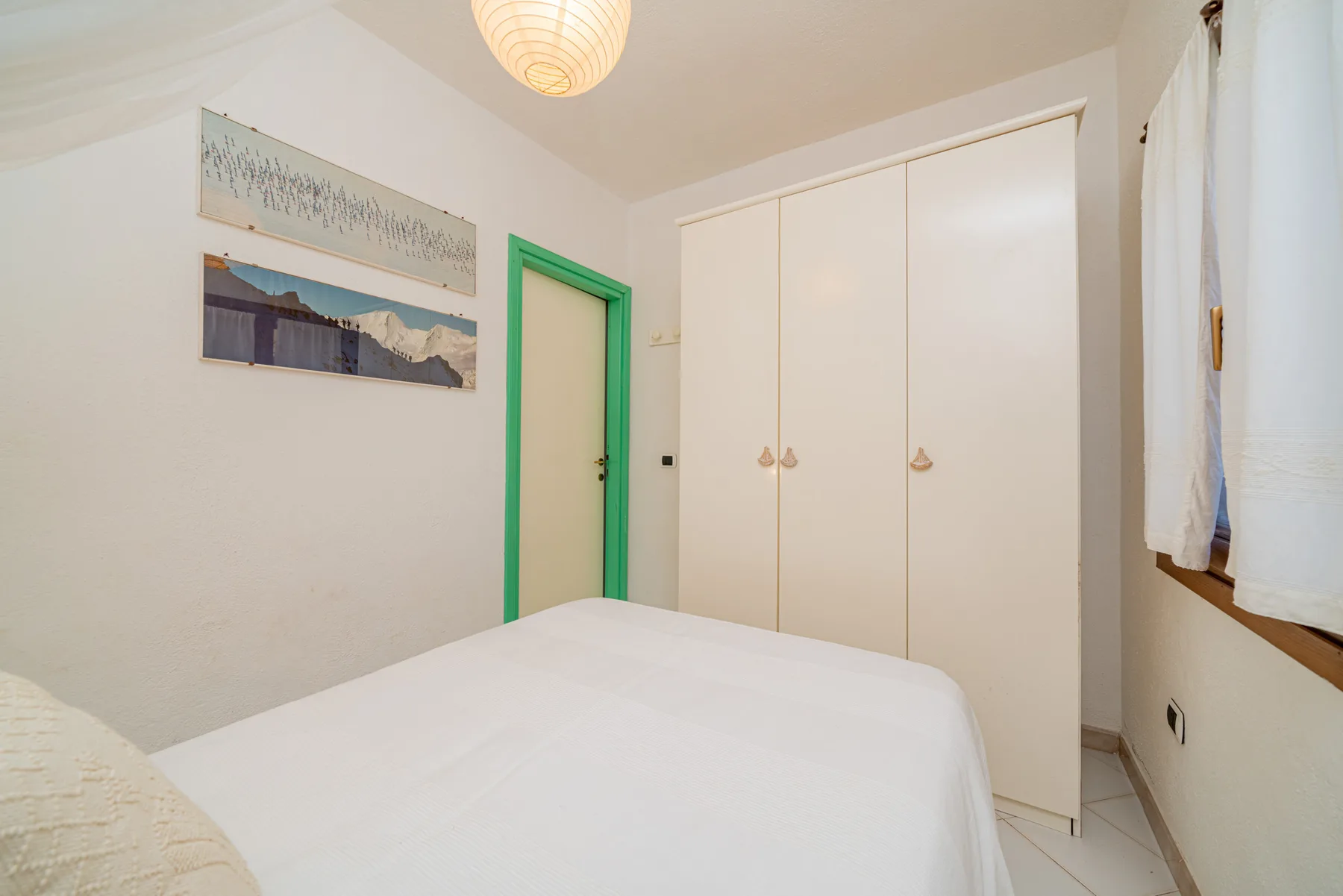 A bedroom with a bed, white wardrobe, and green-trimmed doorway.