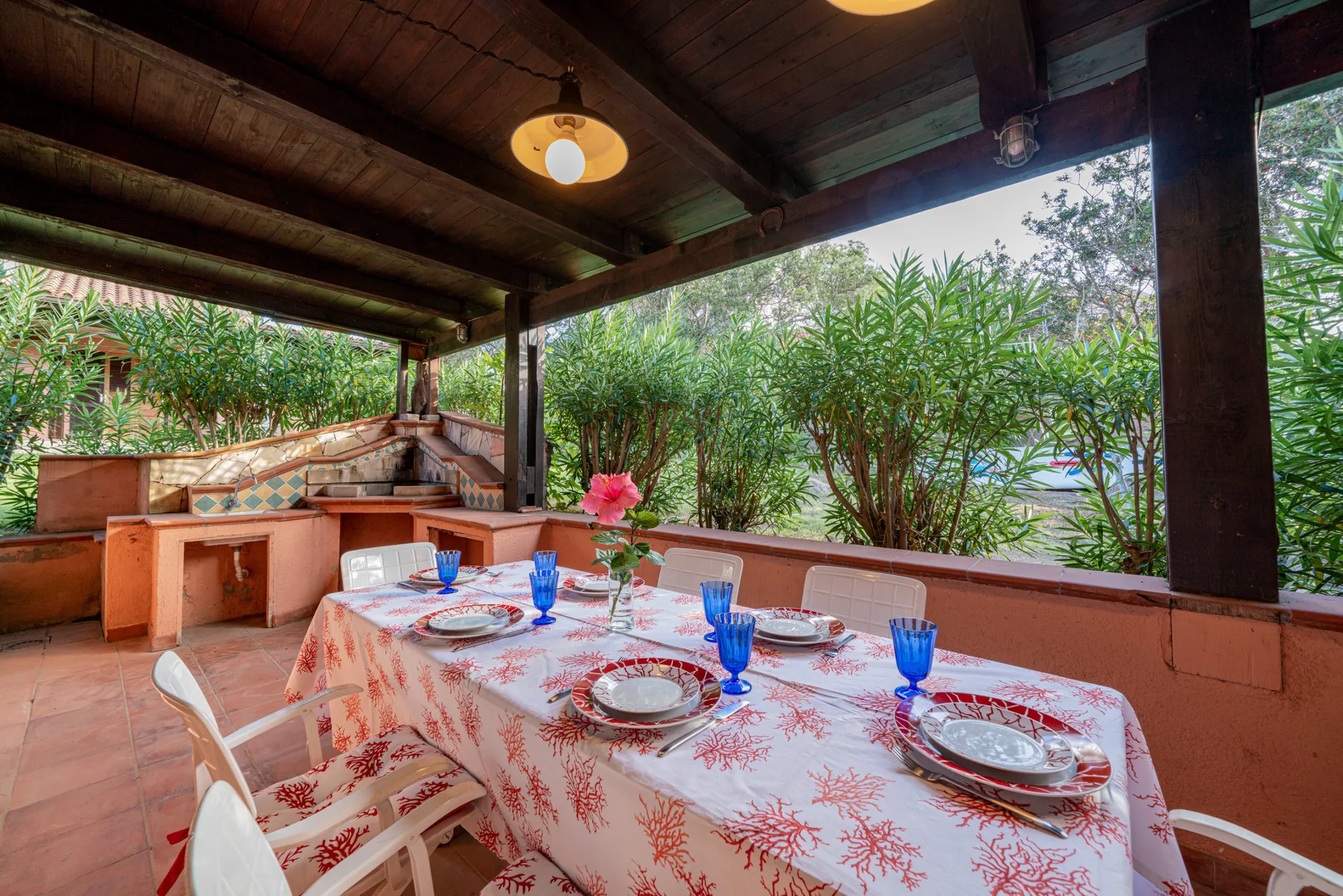 A covered outdoor dining area has a table set with dishes and blue glasses.