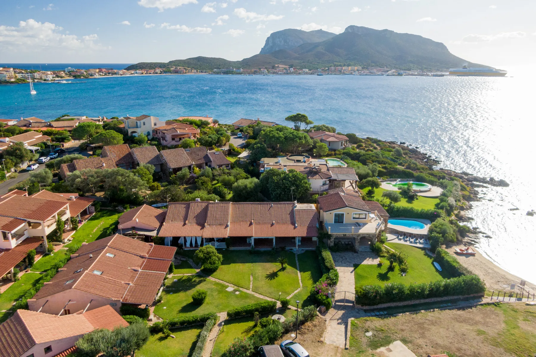 A coastal resort with terracotta-roofed buildings beside a bright blue bay.