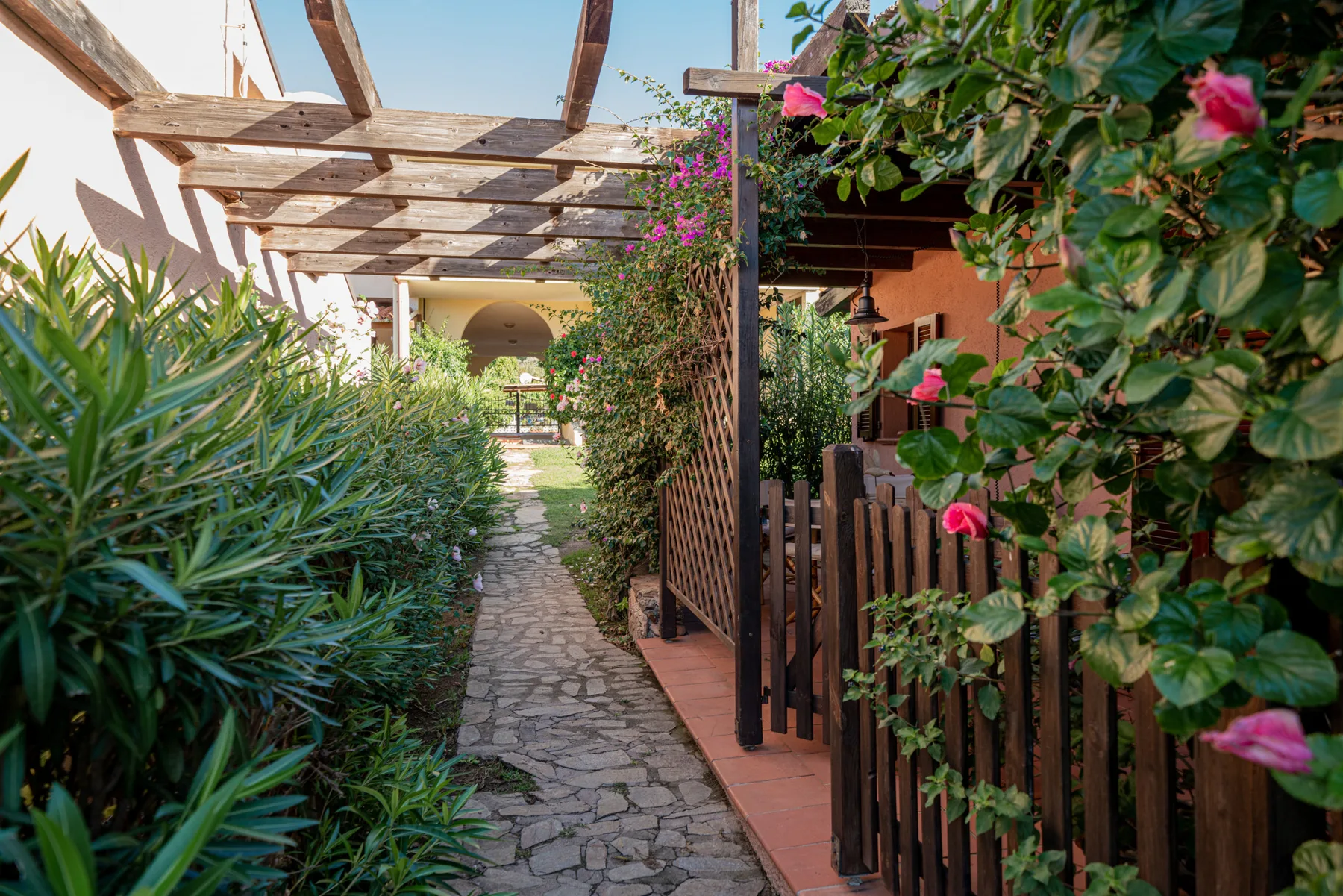 A stone path runs through a leafy garden beside a wooden pergola.