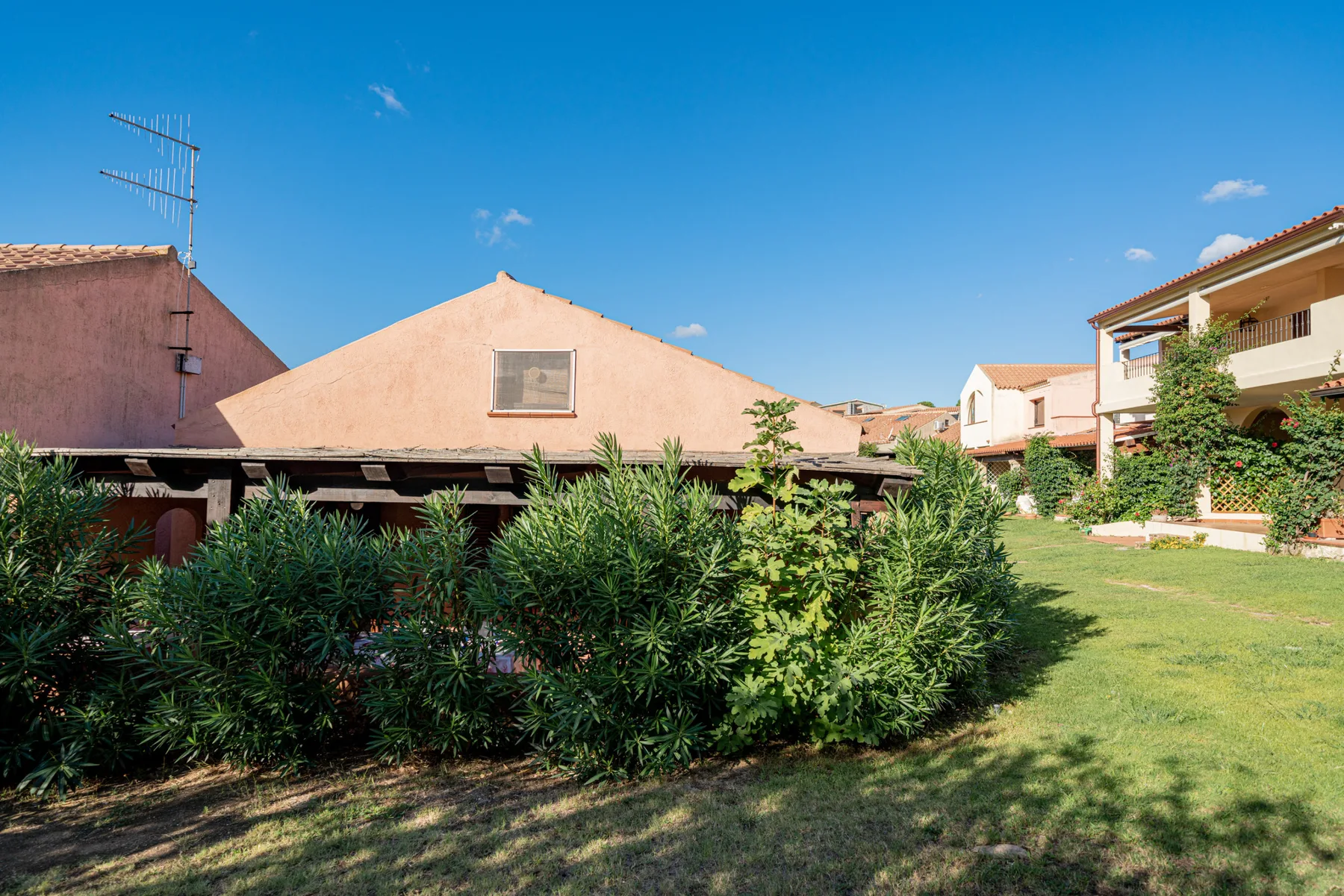 A landscaped courtyard with green shrubs, lawn, and surrounding buildings under a clear sky.